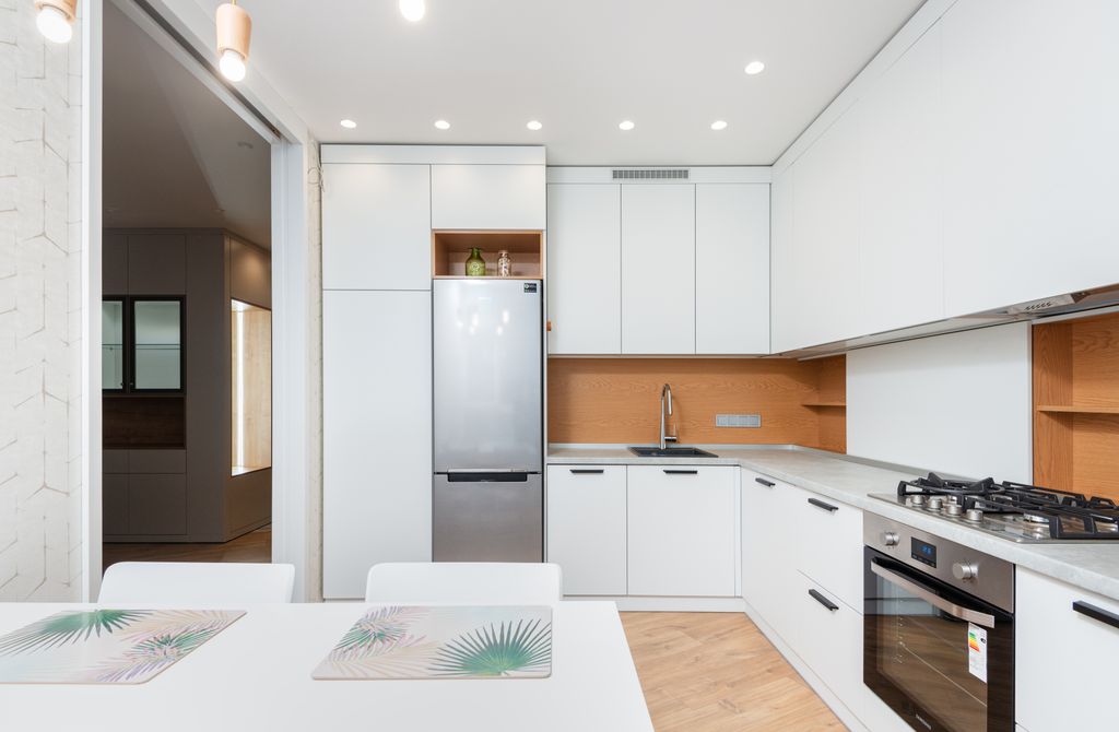 Modern kitchen interior with fridge and cabinets against table with placemats under lamps in house