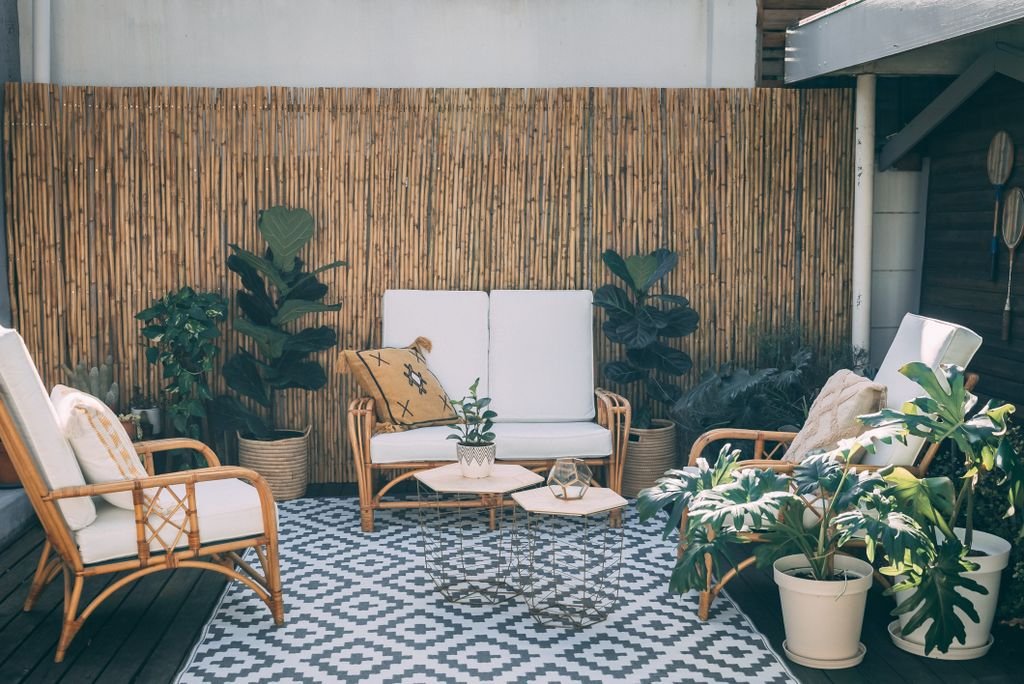 Serene outdoor patio featuring rattan furniture, potted plants, and bamboo decor.